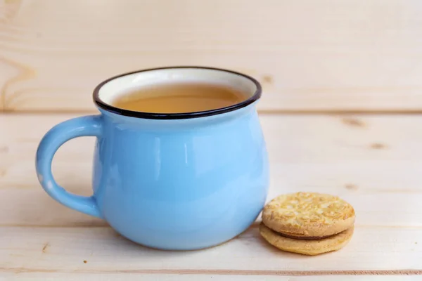 blue mug of tea and sandwich cookies on wooden background