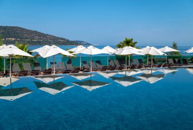 Açık havada lüks yüzme havuzunun etrafında gölgeler olan beyaz şemsiyeler. 