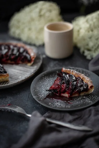 Cozy dark kitchen with flowers and appetizing plum cake with sugar powder.