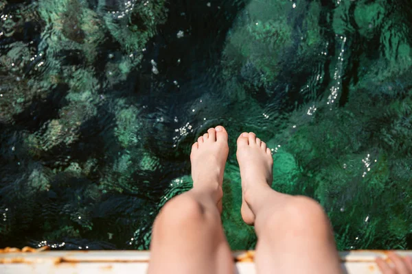 Pair of kid\'s feet on blue sea background with white reflections. View from the top.