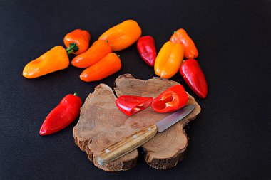 Siyah arka plan ve ahşap plaka tüm ve bıçakla kesilmiş taze parlak kırmızı ve sarı biber