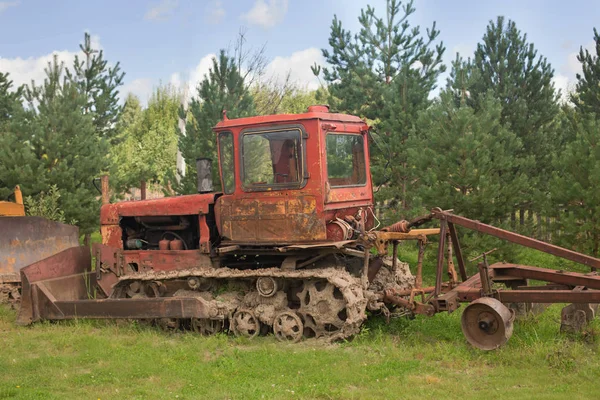 tractor old working farm in the pines and fur-trees in front of a fenc