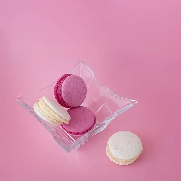 Mehrere mehrfarbige Macarons in einem Glasteller auf einem quadratischen rosa — Stockfoto