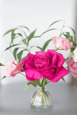 Açık dikey arkaplanda pembe bir gül olan bir buket. Seçici odak, boşluğu kopyala.