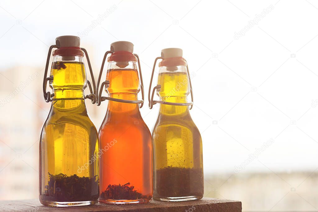 Three bottles of freshly-flavored olive oil with spices on a window in the sun.