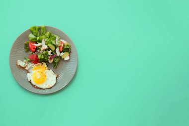 Yeşil arka planda gri tabakta salatalı sahanda yumurta. Seçici odaklanma. Düzen, düz yatış, kopyalama alanı, üst görünüm