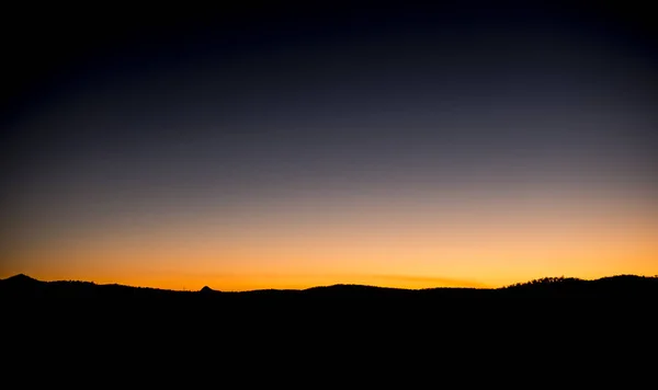 Sunset over silhouetted mountains with a blue and orange sky