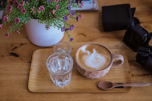 Kopp av cappuccino med latte konst på träplatta, glas vatten — Stockfoto