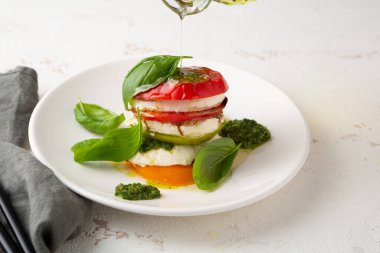 Beyaz tabakta fesleğen soslu Caprese salatası.