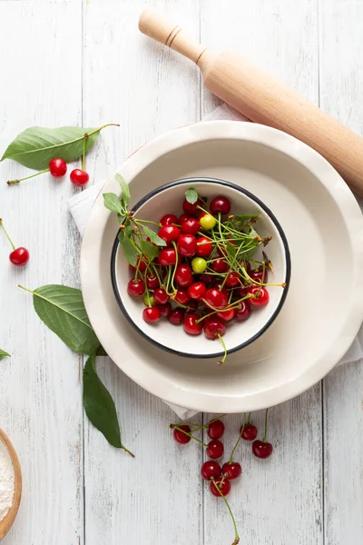 Pie dish and fresh cherry on white wooden surface