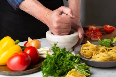 Eller makarna için sos yapıyor, taze malzemeler beyaz masada.