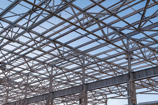 Metal beams at the top of the unfinished steel structure of the building under construction, against the blue sky.