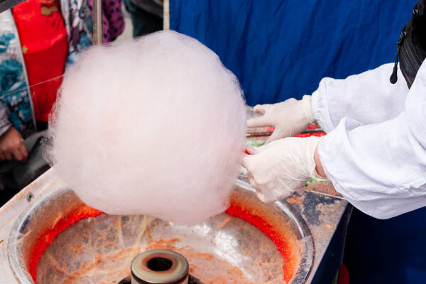 The seller of cotton candy forms a lump for sale.