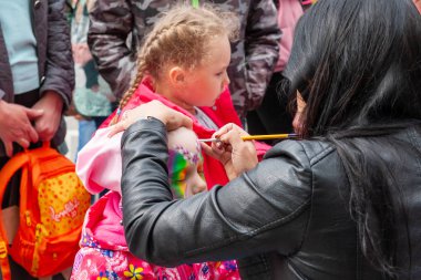 küçük bir kızın yüzünde vücut sanatı, Rusya Günü kutlama. Küçük kızlar vücut sanatı örnekleri ile bir katalog düşünüyor.