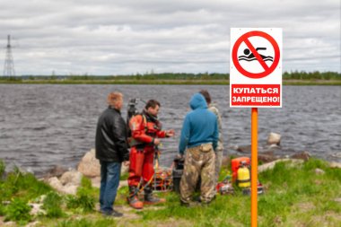 Yazıtla kıyıda uyarı işareti-Yıkanması yasaktır. Arka planda, dalış çalışmaları. 