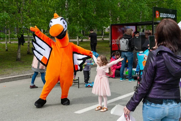 ドードーピッツェリアピザのシンボルであるオレンジ色の鳥の形をした大きな人形が、お祭りで子供たちと一緒に撮影されています。. — ストック写真