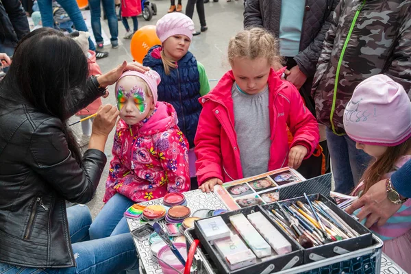 小さな女の子の顔にボディアート、ロシアの日のお祝い。小さな女の子はボディアートのサンプルとカタログを検討しています. — ストック写真