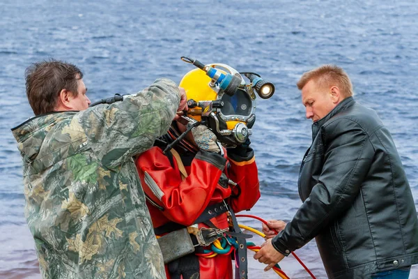 Deux assistants aident le plongeur à mettre un casque. Travaux en eau profonde . — Photo