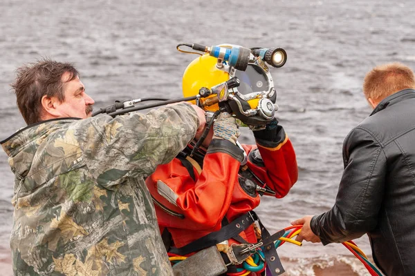 Deux assistants aident le plongeur à mettre un casque. Travaux en eau profonde . — Photo