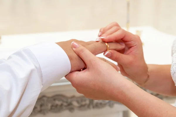 Hands of the bride and groom, close-up. The bride puts the weddi