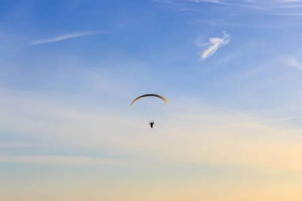 Mavi gökyüzünde kırmızı ve sarı gölgelikli ve yumuşak ince bulutlu tek güçlü paraglider.