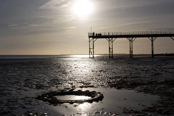 düşük tide sıcak günbatımı, traktör lastiği ön planda ile eski İngiliz Victoria pier adam durdu