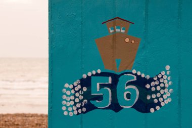 Brown painted boat on on a blue english beach hut with the number 56 and the beach and sea in the background clipart
