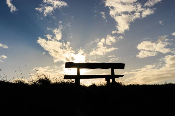 Düşünceli ve barışçıl siluet ahşap bank ve çimenler. Arka planda mavi ve beyaz yumuşacık bir gökyüzü, ışık huzmeleri.