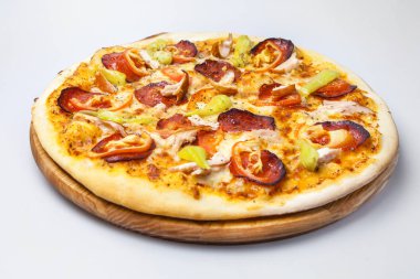 Jambonlu, tavuklu ve biberli sulu peynirli pizza beyaz arka planda yuvarlak bir tahtada.