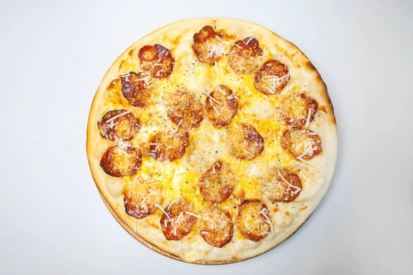 Sosisli, peynirli ve baharatlı yuvarlak pizza masanın ortasındaki ahşap bir tahtanın üzerinde.