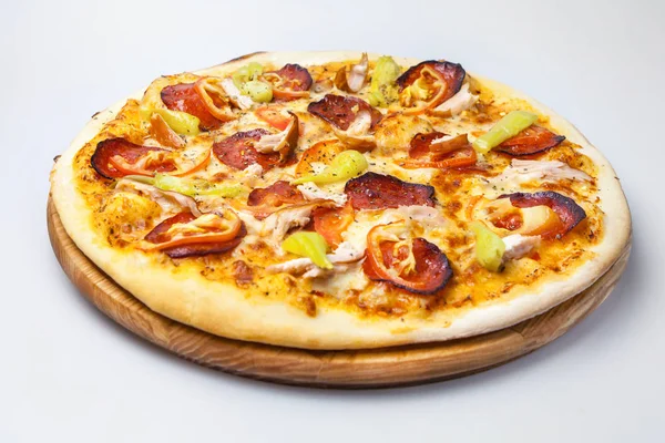 Jambonlu, tavuklu ve biberli sulu peynirli pizza beyaz arka planda yuvarlak bir tahtada.