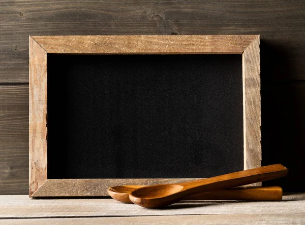 Wooden kitchen cooking tools in front of rustic wooden board background on wood table with empty menu board with copy space