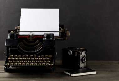 Boş, boş bir kağıt yaprağına, kamera ve siyah arka plan ile ahşap masa üstünde defter ile antika daktilo