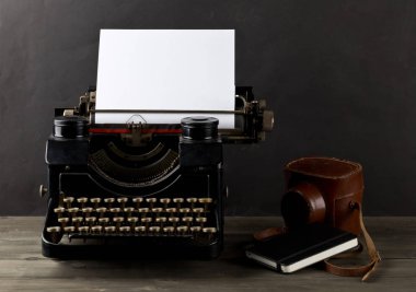 Boş, boş bir kağıt yaprağına, kamera ve siyah arka plan ile ahşap masa üstünde defter ile antika daktilo