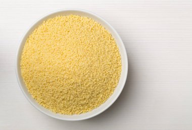 Çiğ, çiğ kuskus Beyaz ahşap zemin üzerinde beyaz kase üst görünümünde yukarıdan yığını