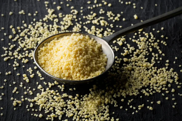 Seçici odak koyu ahşap masa zemin üzerine metal kaşık çiğ, çiğ kuskus yığını