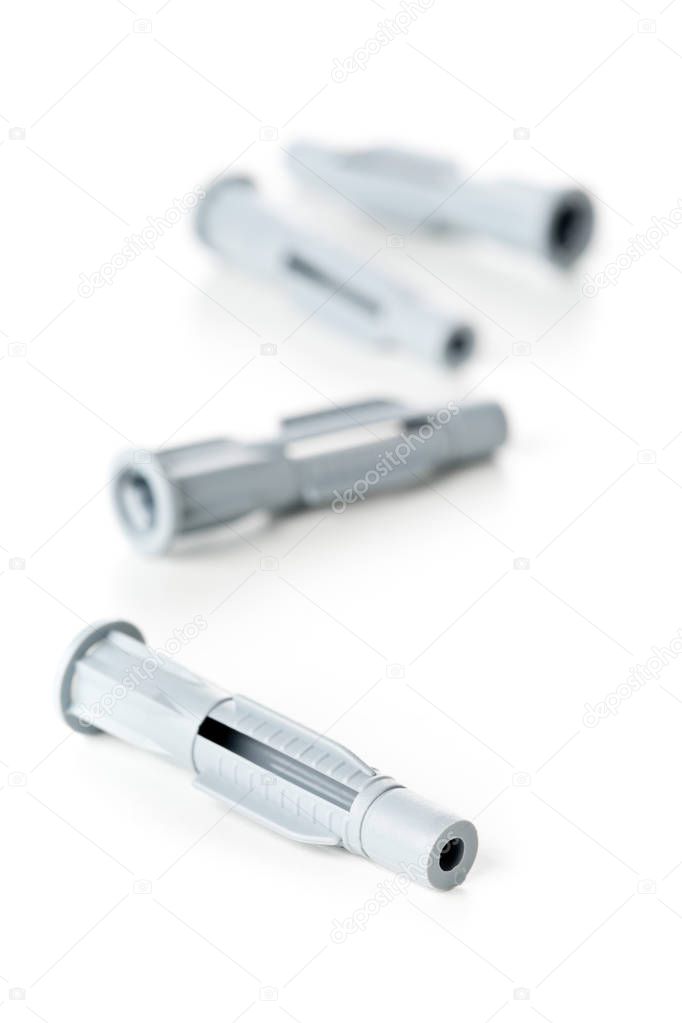 Closeup of new, unused, grey plastic wall plug bolts over white background - selective focus