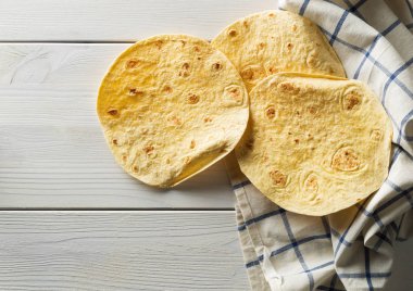 Taze, boş buğday tortilla düz bulaşık bezi üzerinde üstten görünüm Beyaz ahşap masa arka plan üzerinde yatıyordu.