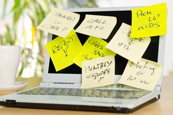 Laptop screen covered with sticky notes with different appointments on brown wooden desk in office - over-worked or too much work concept