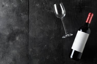 Kopya alanı ile yukarıdan düz koyu ahşap masada boş şarap kadehi ile kırmızı şarap şişesi yatıyordu