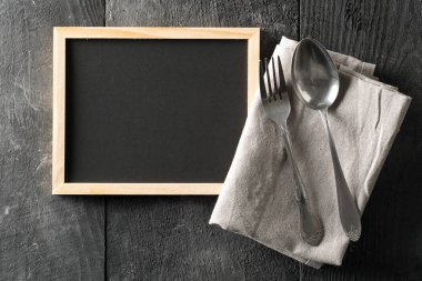 Boş, boş, siyah kara tahta kaşık ve çatal gümüş ve gri kurulama bezi düz ile yukarıdan siyah ahşap tablewith kopya alanı üzerinde yatıyordu