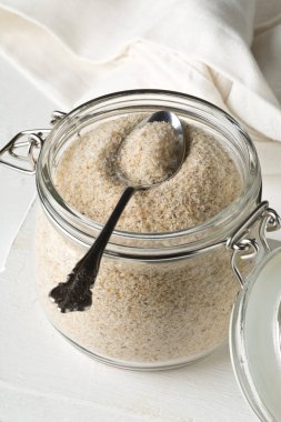 Psyllium kabuğu yığını da beyaz masa arka plan üzerinde metal kaşık ile cam kavanoza isabgol denir. İsabgol olarak da bilinir psyllium kabuğu Hindistan'da bulunan dar ovata bitkisinin tohumlarından elde edilen lif olduğunu. Seçici odak.