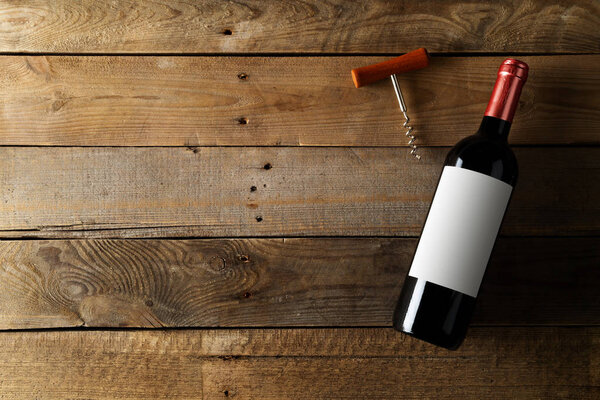 Red wine bottle with corkscrew on brown rustic wooden table flat lay from above with copy space