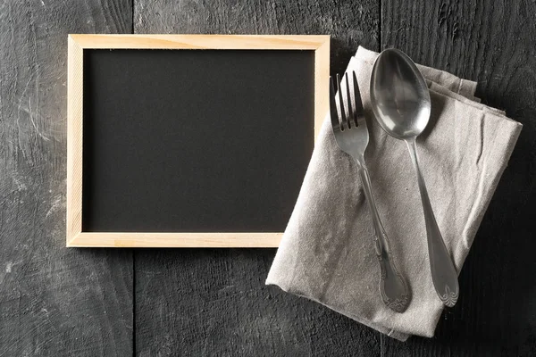 空白的 黑色的黑板 勺子和叉子银器和灰色盘子毛巾平躺在从上面的黑色木桌与复制空间 — 图库照片