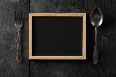 Boş, boş, siyah kara tahta kaşık ve çatal çatal bıçak düz ile yukarıdan siyah ahşap tablewith kopya alanı üzerinde yatıyordu
