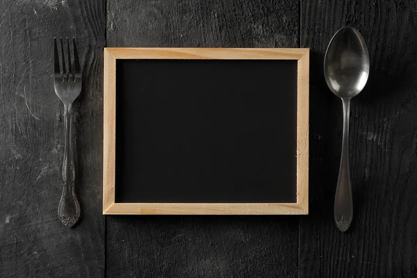 黑色黑板与勺子和叉子银器平躺在从上面的黑色木制桌子与复制空间 — 图库照片