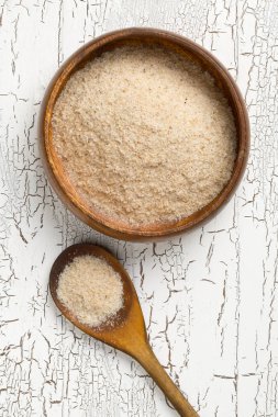 Psyllium kabuğu yığını da beyaz masa arka plan üzerinde ahşap kase ve kaşık isabgol denir. İsabgol olarak da bilinir psyllium kabuğu Hindistan'da bulunan dar ovata bitkisinin tohumlarından elde edilen lif olduğunu. Yukarıdan düz yatıyordu.