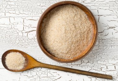 Psyllium kabuğu yığını da beyaz masa arka plan üzerinde ahşap kase ve kaşık isabgol denir. İsabgol olarak da bilinir psyllium kabuğu Hindistan'da bulunan dar ovata bitkisinin tohumlarından elde edilen lif olduğunu. Yukarıdan düz yatıyordu.