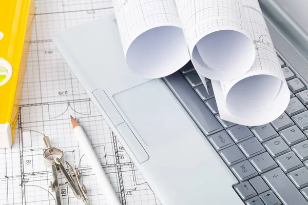 Rolls of architectural blueprint house building plans on laptop