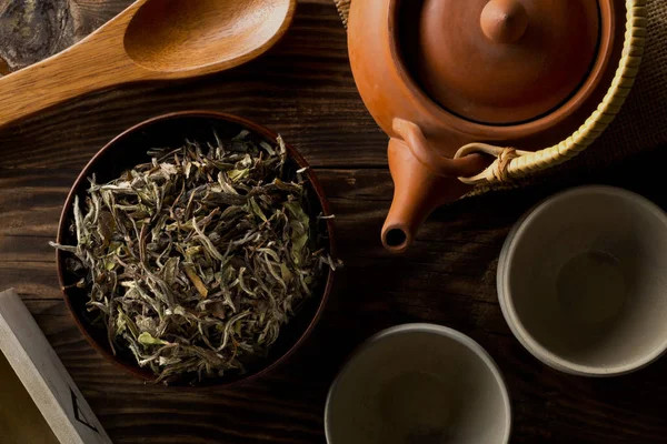 Tas de feuilles de thé blanc séchées et crues dans un bol en bois avec théière a — Photo
